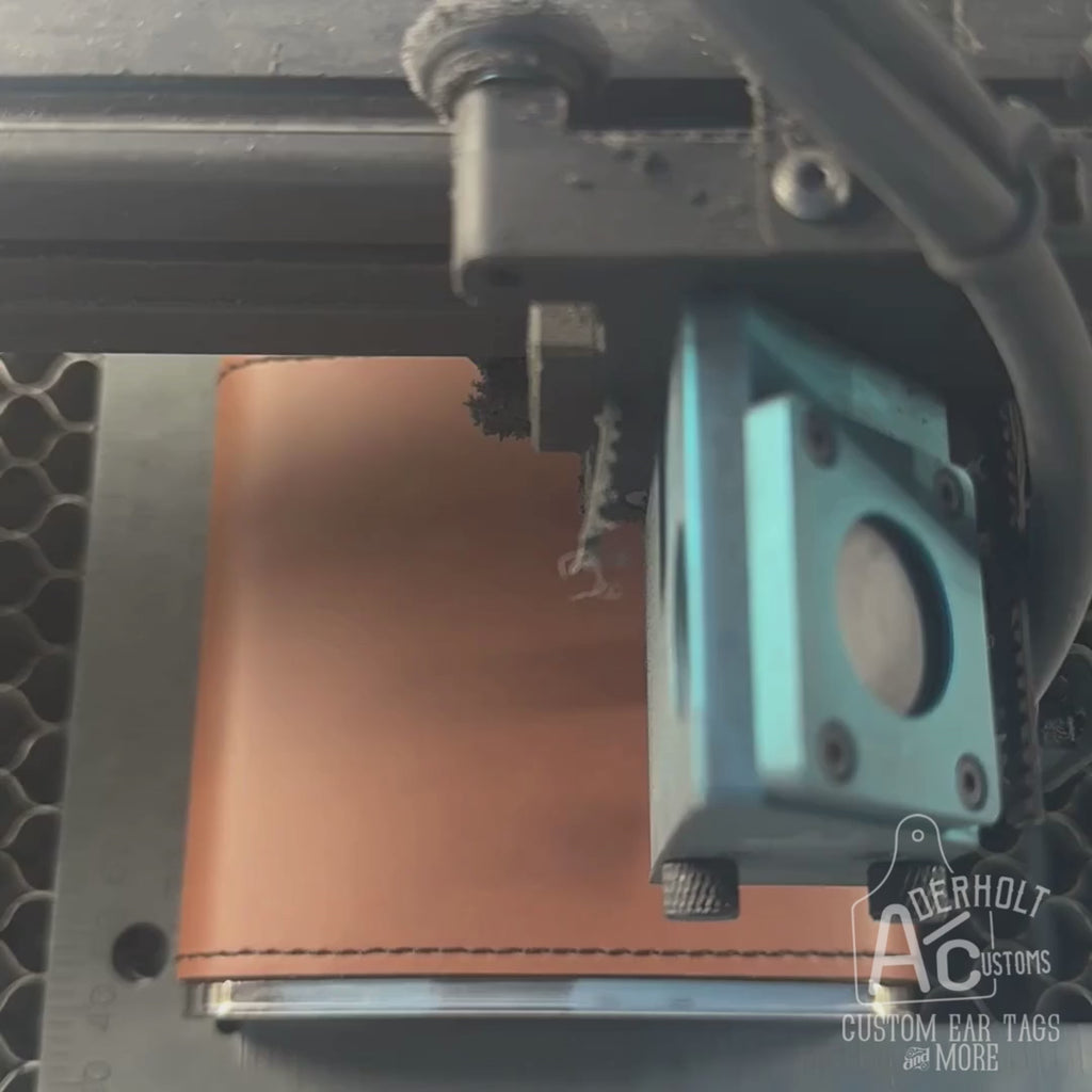 A laser engraver engraving a custom brand on a leatherette wrapped flask. 